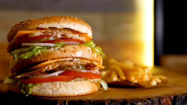 一个大的双层鸡肉汉堡放在一块木板上，旁边是炸薯条。专业烹饪的快餐。视频下载