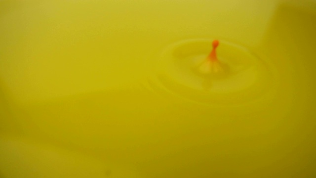 微距摄影的黄色涂料背景。在慢镜头中，橙色的颜料滴在黄色的颜料上。视频下载