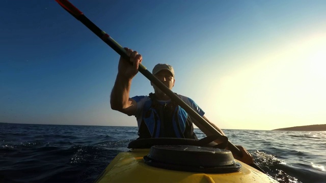 在傍晚的阳光下，一名男子在海上划着皮艇视频素材