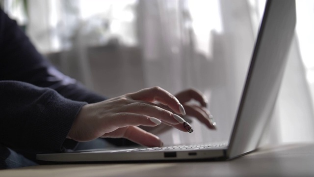 在窗帘正在显影的背景下，一个女人在家里的笔记本电脑上用手打字视频素材