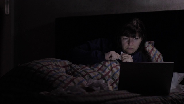 郁闷的女人晚上躺在床上靠近笔记本电脑，生气的女人视频下载