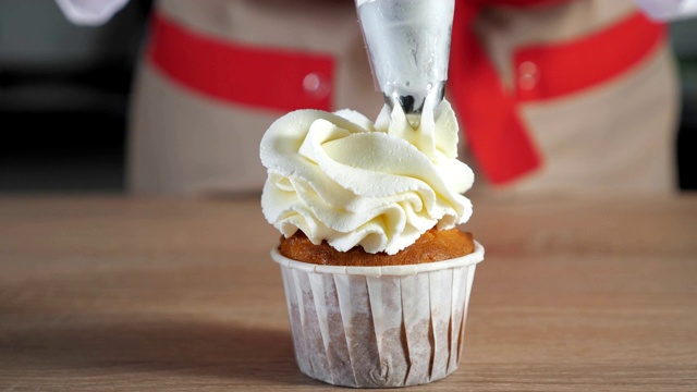 糕点师将松饼装饰在纸杯，白色奶油和糕点袋。视频素材