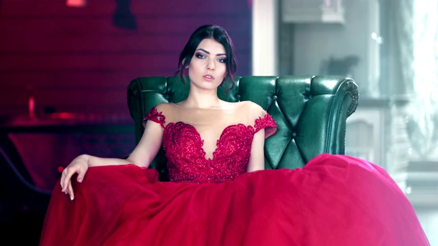 性感的时尚女人的肖像在红色的晚礼服魅力的衣服坐在扶手椅上看着相机视频素材