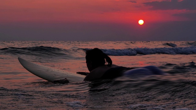 剪影快乐美丽性感的冲浪女孩在冲浪板上等待海浪。在日落的海滩上。运动Cinemagraphs，假期-股票视频素材