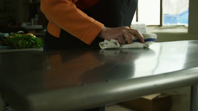 一位年长的白人妇女在一个商业厨房里用洗碗布清洗不锈钢台面视频下载