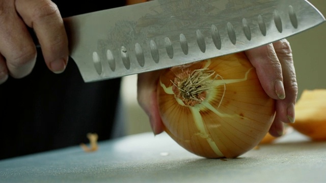 一位年长的白人妇女用菜刀在切菜板上切洋葱视频素材