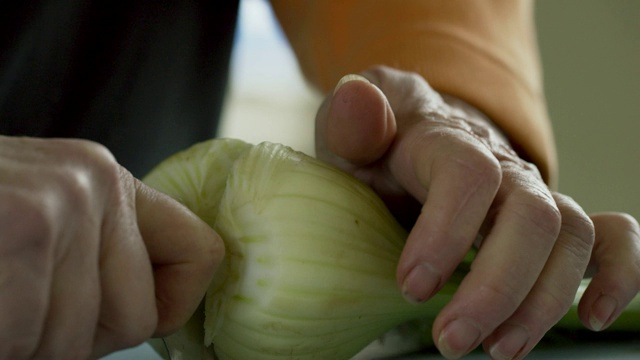一位年长的白人妇女从盛满蔬菜的金属碗里拿出茴香，然后用菜刀将其切在切菜板上视频素材