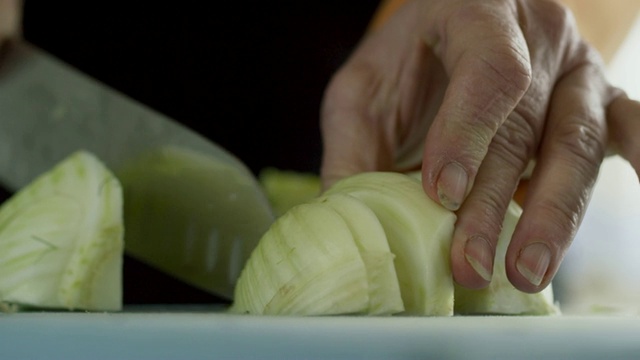 一位年长的白人妇女用菜刀在菜板上切茴香视频素材