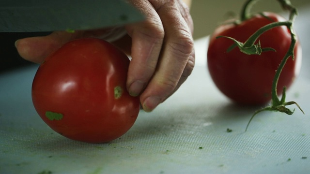 一位年长的白人妇女用菜刀在切菜板上切西红柿视频素材
