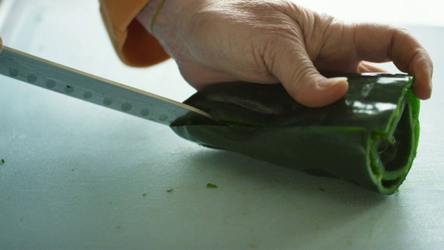 一位年长的白人妇女用菜刀在切菜板上切并清洗波布拉诺辣椒视频素材