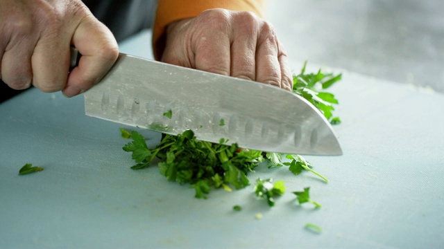 一位年长的白人妇女用菜刀在切菜板上切香菜视频下载