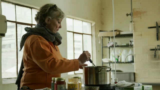 一位六十多岁的白人妇女在一间商业厨房里用不锈钢炖锅搅拌食物视频素材