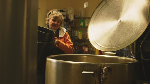 一名六十多岁的白人妇女从一个五加仑的水桶里往一个大型金属储存罐里倒水视频素材