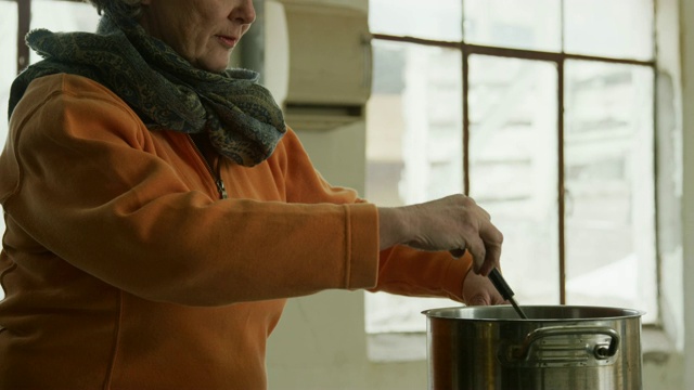 一位六十多岁的白人妇女在一间商业厨房里用不锈钢炖锅搅拌食物视频素材
