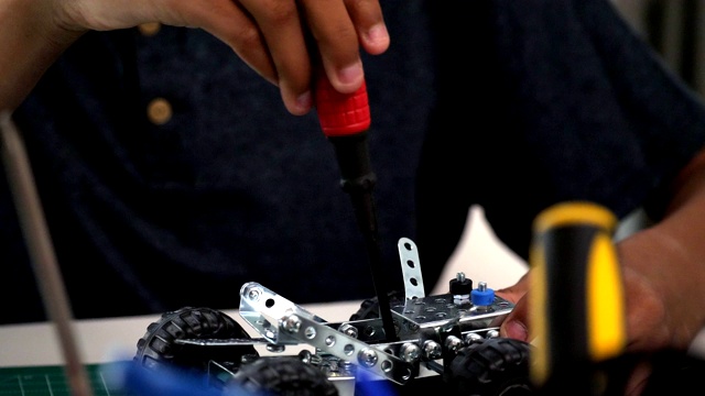 一个十几岁的男孩正在用螺丝刀制造机器人视频素材