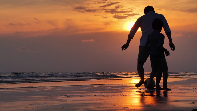 剪影快乐的父亲和儿子玩足球在沙滩上日落。快乐的一家人在海滩上享受暑假。假日旅行的概念。假期——iStock视频素材