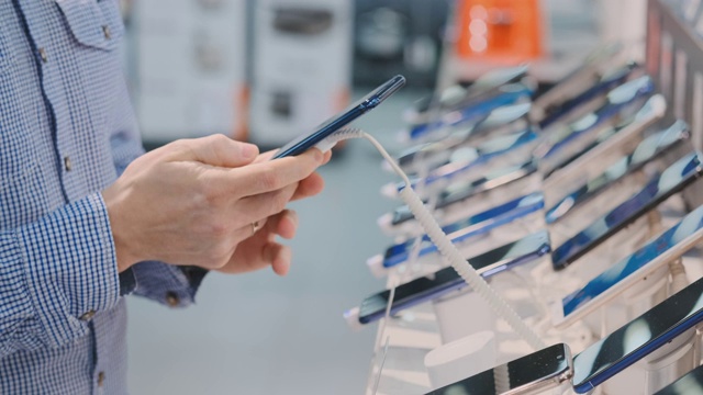 一个男人的手的特写正在选择购买一个新的智能手机在一个电子商店的店面附近视频素材