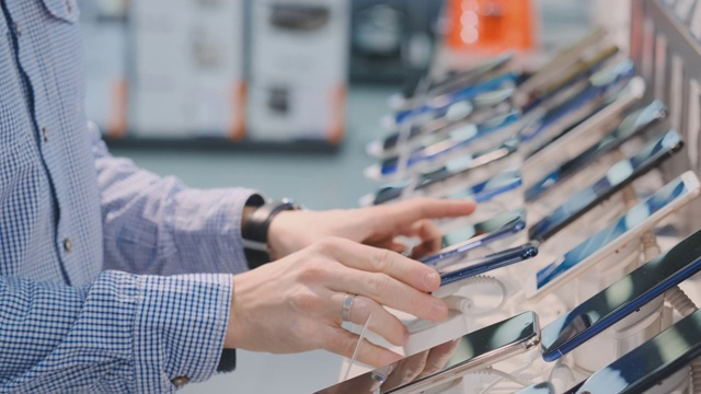 一个男人的手的特写旋转和检查在一个现代电子商店的新智能手机的设计。买手机前先拿着视频素材