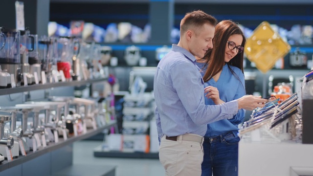 一对幸福的家庭夫妇，男人和女人站在柜台上的手机在休闲衣服选择一个新的智能手机在现代电子商店视频素材