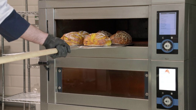 面包师用皮从烤箱中取出刚烤好的面包的侧面图。在面包店烤面包。烹饪食物的概念视频下载