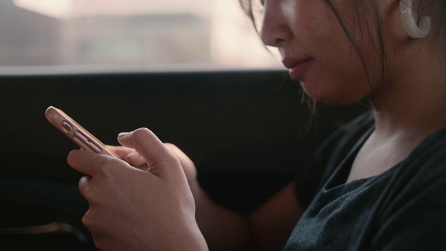 年轻女子在汽车后座上用智能手机打字。视频素材