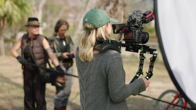 SLO MO.电影摄影师持有相机钻机，而吊杆操作员和音效混音站在背景与所有女性工作人员。视频下载
