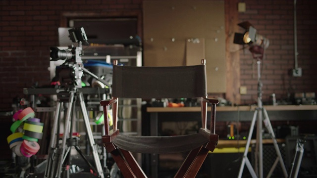 SLO MO:在一个独立的电影片场，一个空导演的椅子坐在一个摄像机三脚架和一个灯架之间。视频下载