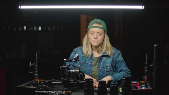 这是一幅自信的女摄影师在工作台上安装新镜头，抬头对着镜头微笑的照片。视频素材