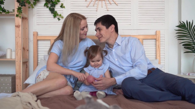 微笑的一家人在床上，爸爸妈妈和他们的小女儿玩玩具。视频下载