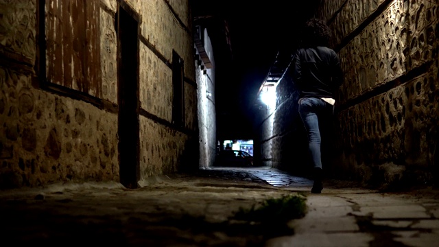 一个女人的剪影，走在古老的黑暗小巷的石头路面和墙壁晚上。保加利亚班斯科的老房子和街道建筑视频素材