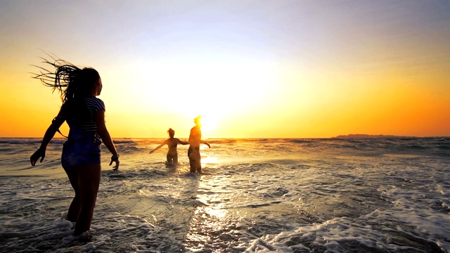 一群快乐的少女在日落的海滩上玩水。美丽快乐的青少年朋友们玩，跳舞和喷洒在夏季日落。太阳耀斑。缓慢的运动。夏季视频素材