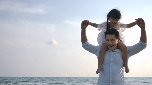 快乐的爸爸和女儿在蓝天背景下的海滩上玩耍。缓慢的运动。幸福的家庭的概念。视频素材