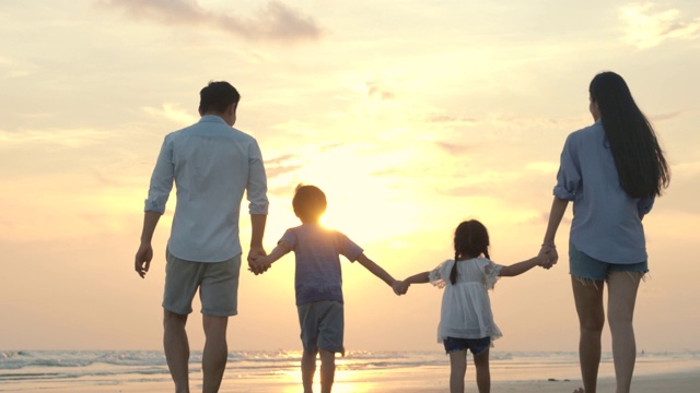 快乐的亚洲家庭漫步在夏日日落的海滩上。缓慢的运动。家庭，假期和旅游的概念。视频下载