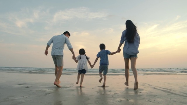 慢镜头-日落时分，亚洲家庭在海滩上奔跑，心情愉快。家庭，假期和旅游的概念。后视图。视频购买