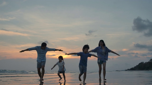 剪影快乐的亚洲家庭玩和有乐趣的海滩上日落。缓慢的运动。家庭、自由和旅行的概念。视频素材