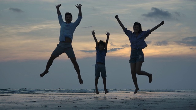 在夕阳的背景下，欢乐的一家人在海滩上跳跃的剪影，慢镜头。家庭、自由和旅行的概念。视频素材
