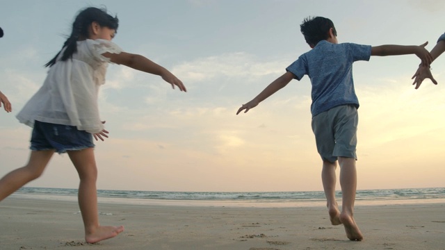 慢镜头-日落时分，亚洲家庭在海滩上奔跑，心情愉快。家庭，假期和旅游的概念。后视图。视频素材