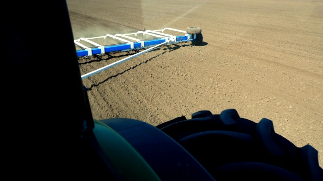 近距离观看，从驾驶室的中耕机，拖拉机上的大轮犁，耙土用大型金属犁，扬起大量的灰尘在可耕地上，肥沃的农田。-为播种准备土壤。春天耕作视频素材