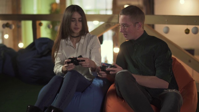 年轻男女坐在咖啡厅舒适的椅子上玩电子游戏。视频下载