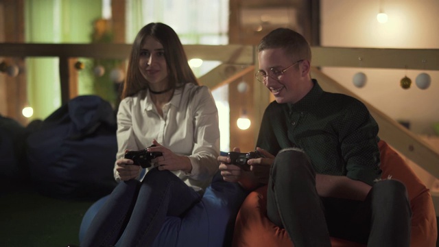 年轻男女坐在咖啡厅舒适的椅子上玩电子游戏。视频素材