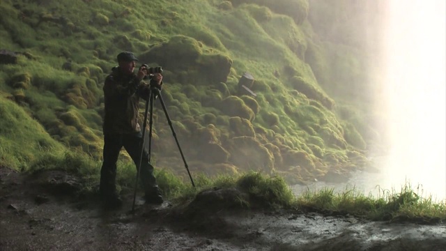 男子在Seljalandsfoss瀑布后面拍照。编辑只使用。视频下载