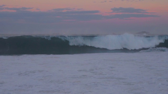 慢镜头:海浪在蓝色的海洋中形成和撞击，上面是粉红色的天空视频素材