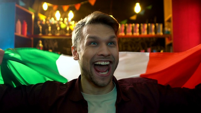 酒吧里兴高采烈的球迷挥舞着意大利国旗，庆祝国家队的胜利视频素材
