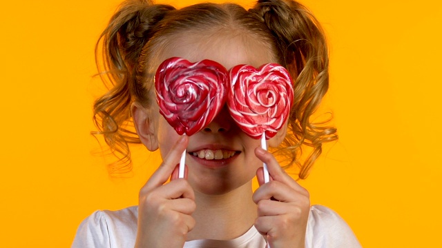 微笑的小女孩开心地闭上眼睛吃心形棒棒糖的童年视频下载