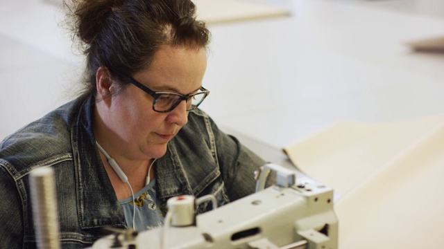 一名四十多岁的白人妇女在室内制造设施中使用工业缝纫机缝制织物视频素材