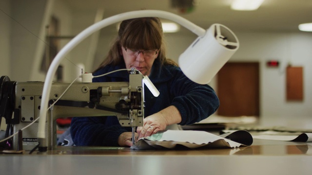 一名五十多岁的白人妇女在室内制造设施中使用工业缝纫机缝制织物视频素材