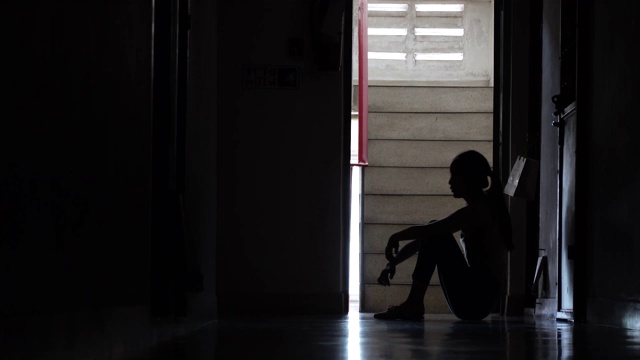 一个悲伤的年轻女孩的剪影坐在黑暗中靠在旧公寓的墙，家庭暴力，家庭问题，压力，暴力，抑郁和自杀的概念。视频素材
