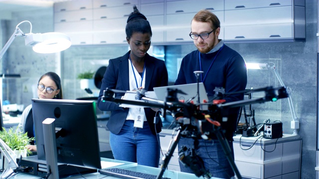 白人男性和黑人女性工程师在一个无人机项目的帮助下笔记本电脑和做笔记。他在一个明亮的现代化高科技实验室工作。视频素材
