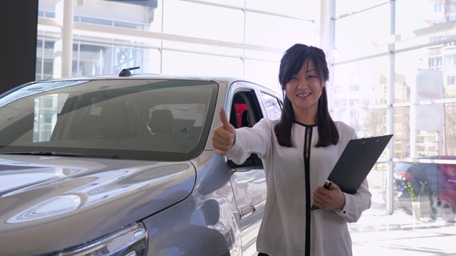 在汽车中心的一辆新车附近，一名女经理微笑着竖起大拇指视频下载