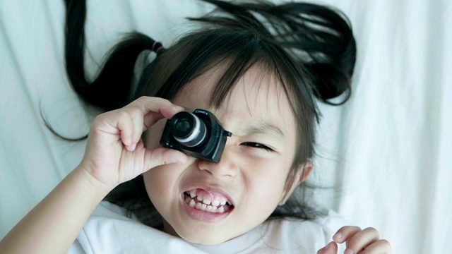 可爱的小女孩周末在床上玩相机，带着积极的情绪视频素材